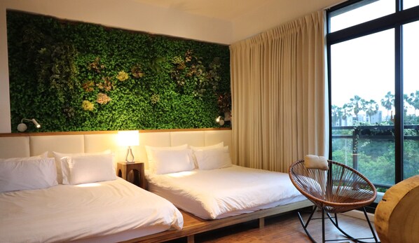 A hotel room with two beds, a green wall, a window with curtains, and a wicker chair.