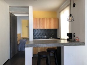 Compact kitchen with central island, black countertop, and pendant light.