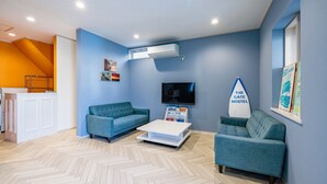 A modern living room with two teal sofas, a white coffee table, and a mounted TV. An air conditioning unit is visible on the wall. - The Gate Hostel Shonan Fujisawa (Fujisawa)