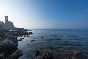 A coastal scene with a historic building featuring a bell tower, rocky shoreline, and calm sea.