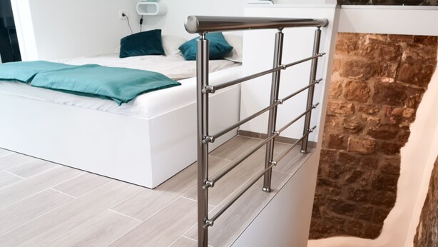 A modern bedroom with a bed, a metal railing, and a stone fireplace. - Korala Apartments (Piran)