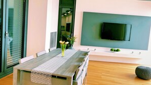 A modern dining area with a wooden table, a vase of flowers, and a television mounted on the wall. - Luxury Sea View Apartment (Koper)