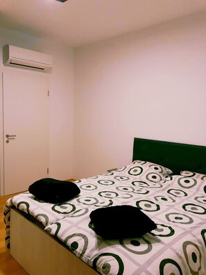Quarto com cama, cabeceira verde e ar condicionado na parede.