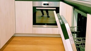 A compact kitchen with a built-in oven and dishwasher, wooden flooring, and light-colored cabinetry. - Luxury Sea View Apartment (Koper)