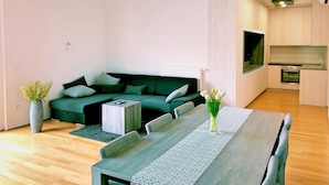 A modern living room with a green sofa, a dining table, and a kitchen area with wooden cabinets and a built-in oven. - Luxury Sea View Apartment (Koper)