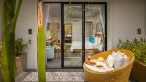 Habitación de hotel moderna con puerta de vidrio que da a un balcón, zona de comedor y dormitorio con cama y almohadas.