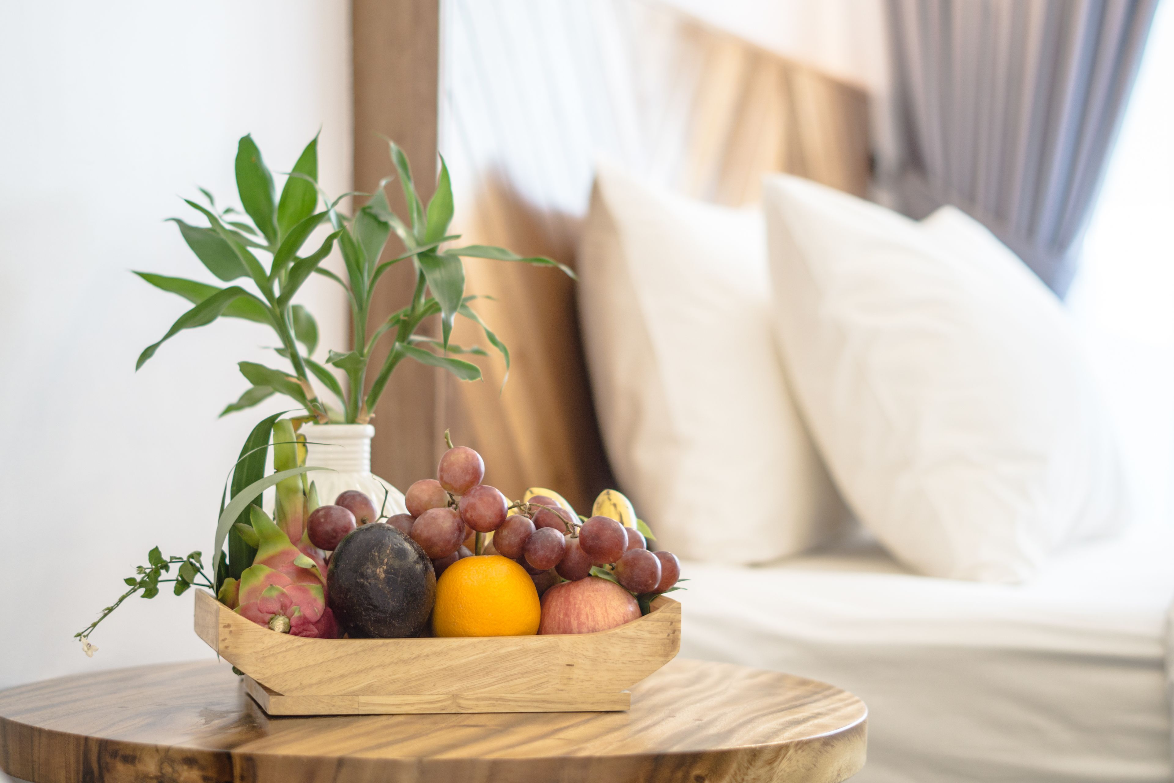 Uma tigela de madeira com uvas, uma maçã e uma banana sobre uma mesa de madeira redonda.