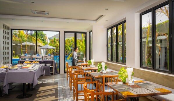 Restaurante com várias mesas, área de buffet e grandes janelas com vista para o exterior.