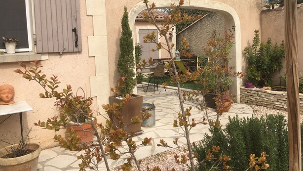 A courtyard with a tiled floor, potted plants, a table, and a chair. - 2 Chambres Tramontane et Alizé (Jonquerettes)