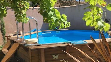 A wooden deck with a pool, surrounded by a wall and trees.