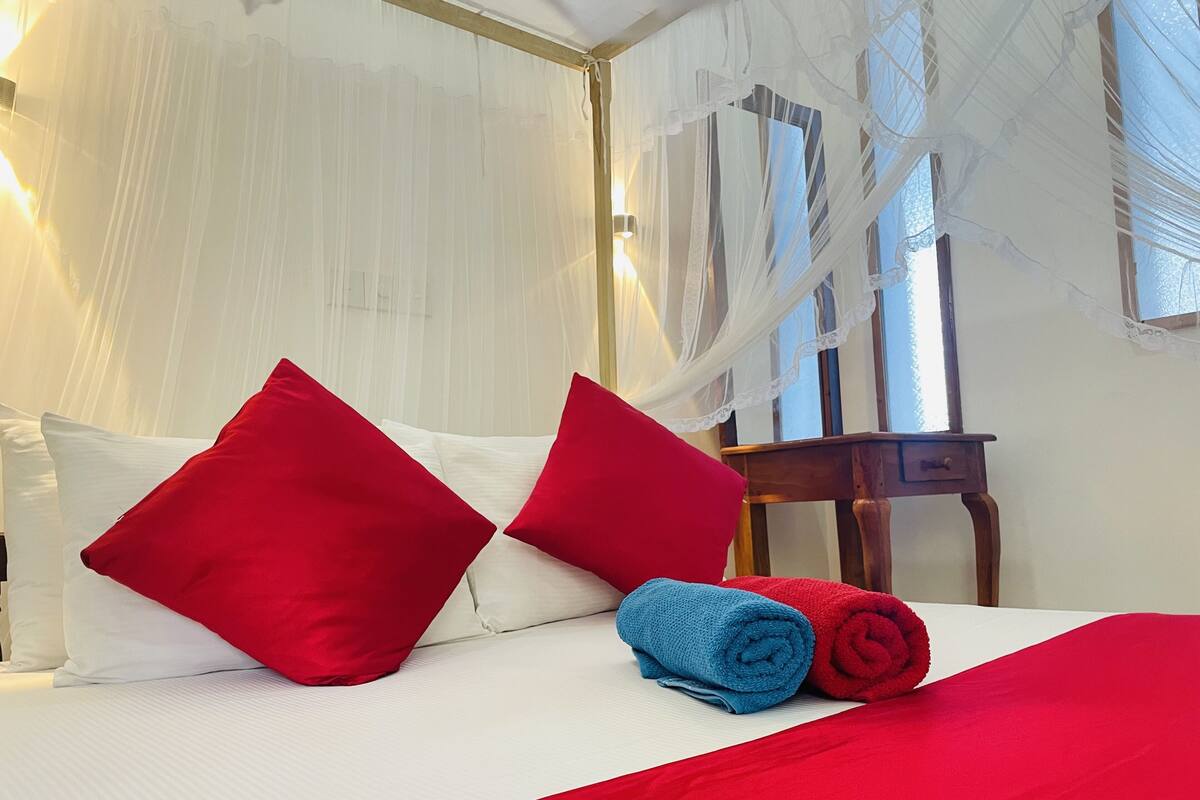 Een keurig opgemaakt bed met witte en rode kussens, een blauwe handdoek en een rode deken.