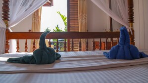 A bed with a canopy, a wooden headboard, and a view of greenery outside. - Cinnamon City (Hikkaduwa)