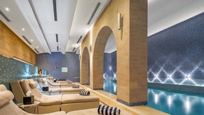 Un spa moderne doté de plusieurs fauteuils inclinables, d’une piscine et d’un mur décoré de mosaïques bleues.