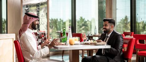 Two people dining at a table with a view of greenery outside.