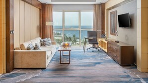 A hotel room with a large window offering a view of the ocean, a sofa, a desk with a chair, and a television on the wall. - The Venue Jeddah Corniche (Jeddah)