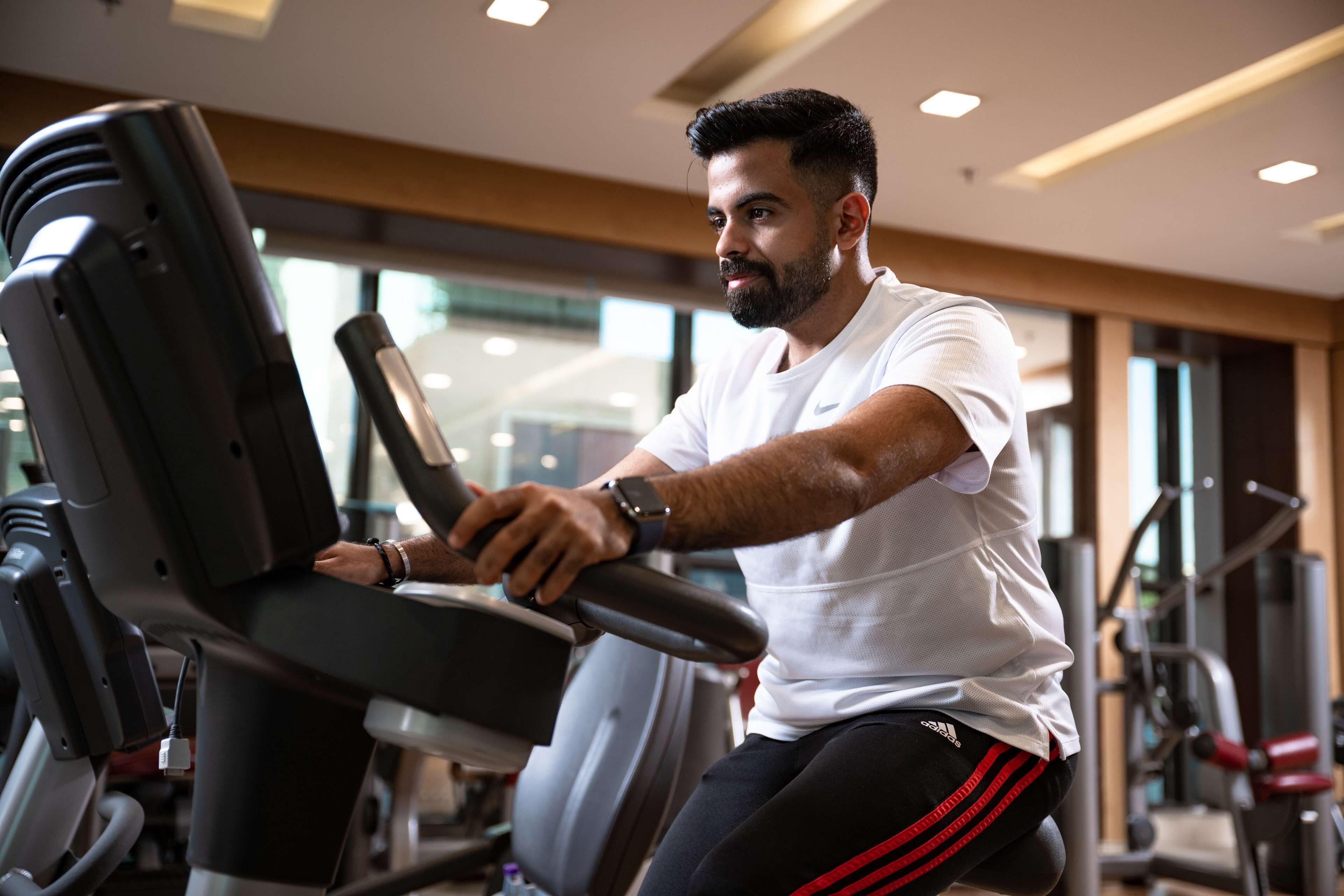 Una persona usando una bicicleta estática en un gimnasio con diversos equipos de ejercicio al fondo.