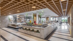 Un hall d’hôtel moderne doté d’un buffet central, d’un sol en marbre et d’un plafond en bois agrémenté de lucarnes.