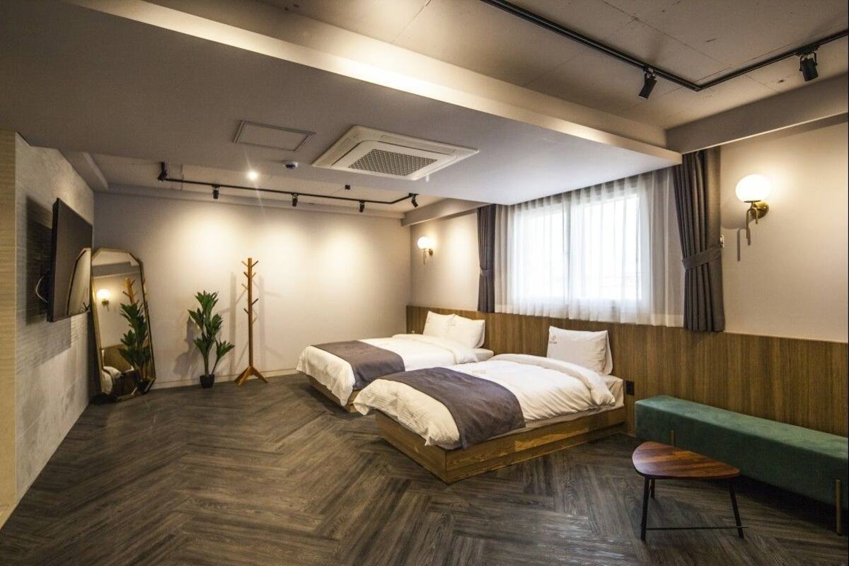 A modern hotel room with a large bed, a green bench, and a mirror on the wall.