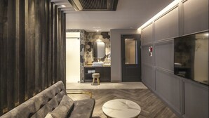 A modern interior with a sofa, a round table, and a bathroom visible in the background. - Hotel Crape Gyeongsan (Gyeongsan)