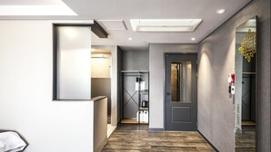 A modern hotel corridor with a wooden floor, a reception desk, a coat rack, and a door leading to a room. - Hotel Crape Gyeongsan (Gyeongsan)