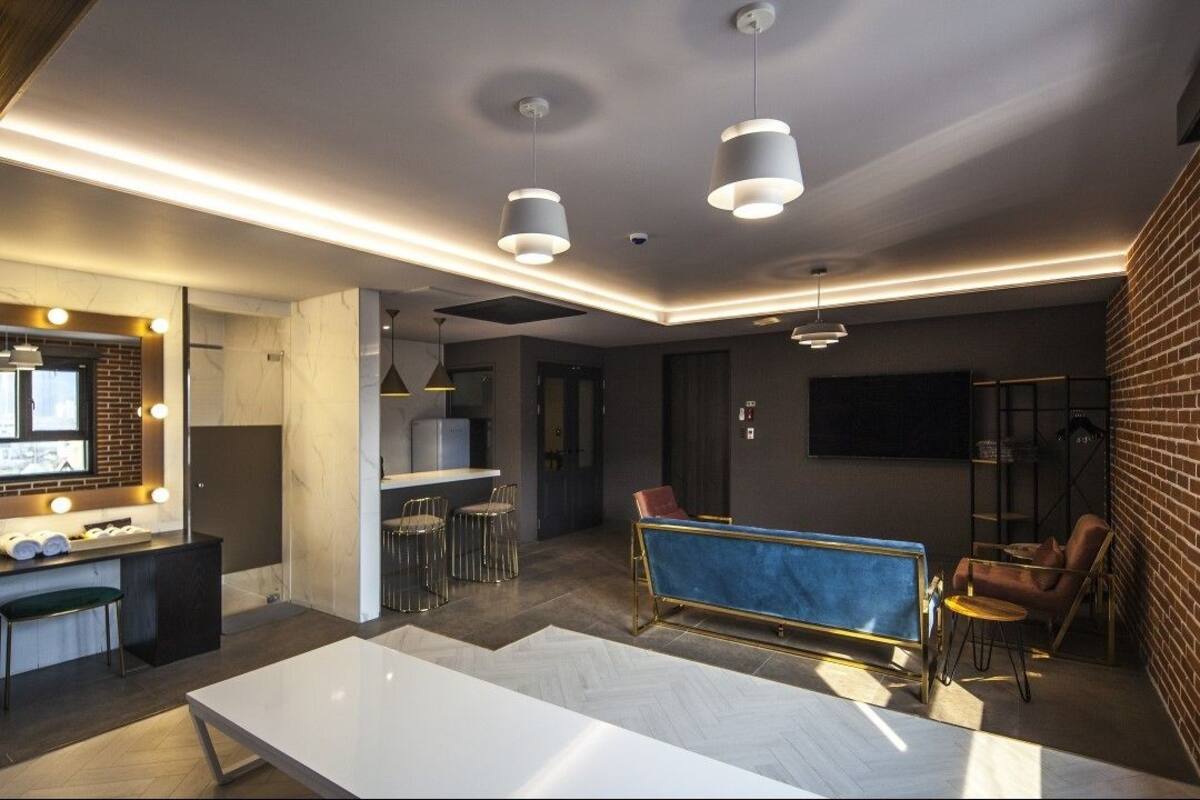 A modern hotel room with a marble-tiled floor, a large white table, a blue sofa, and a brick accent wall.