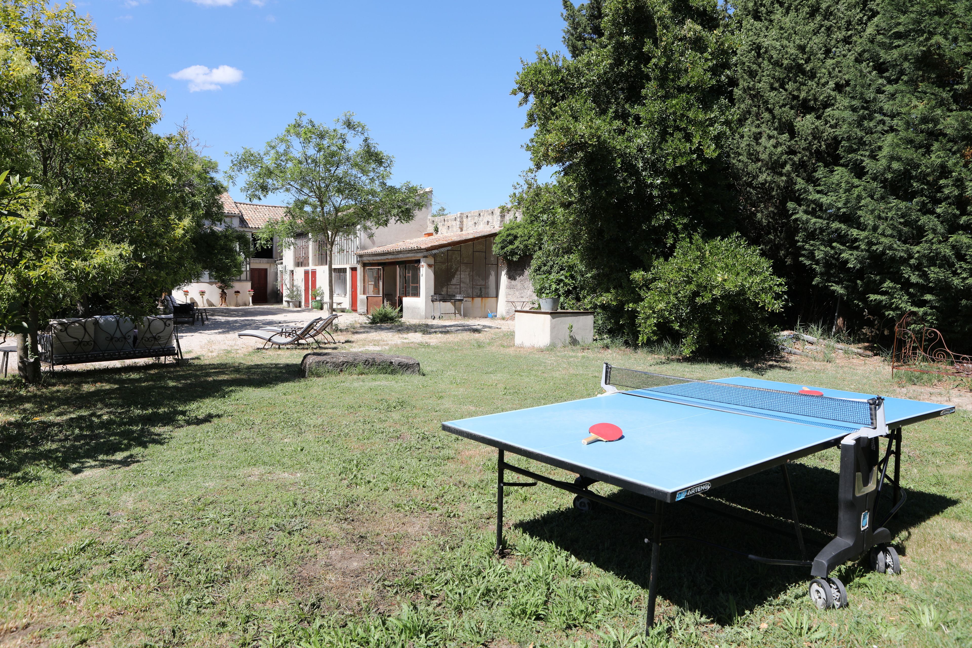 Mesa de ping pong al aire libre en un área con césped, árboles y un edificio al fondo.