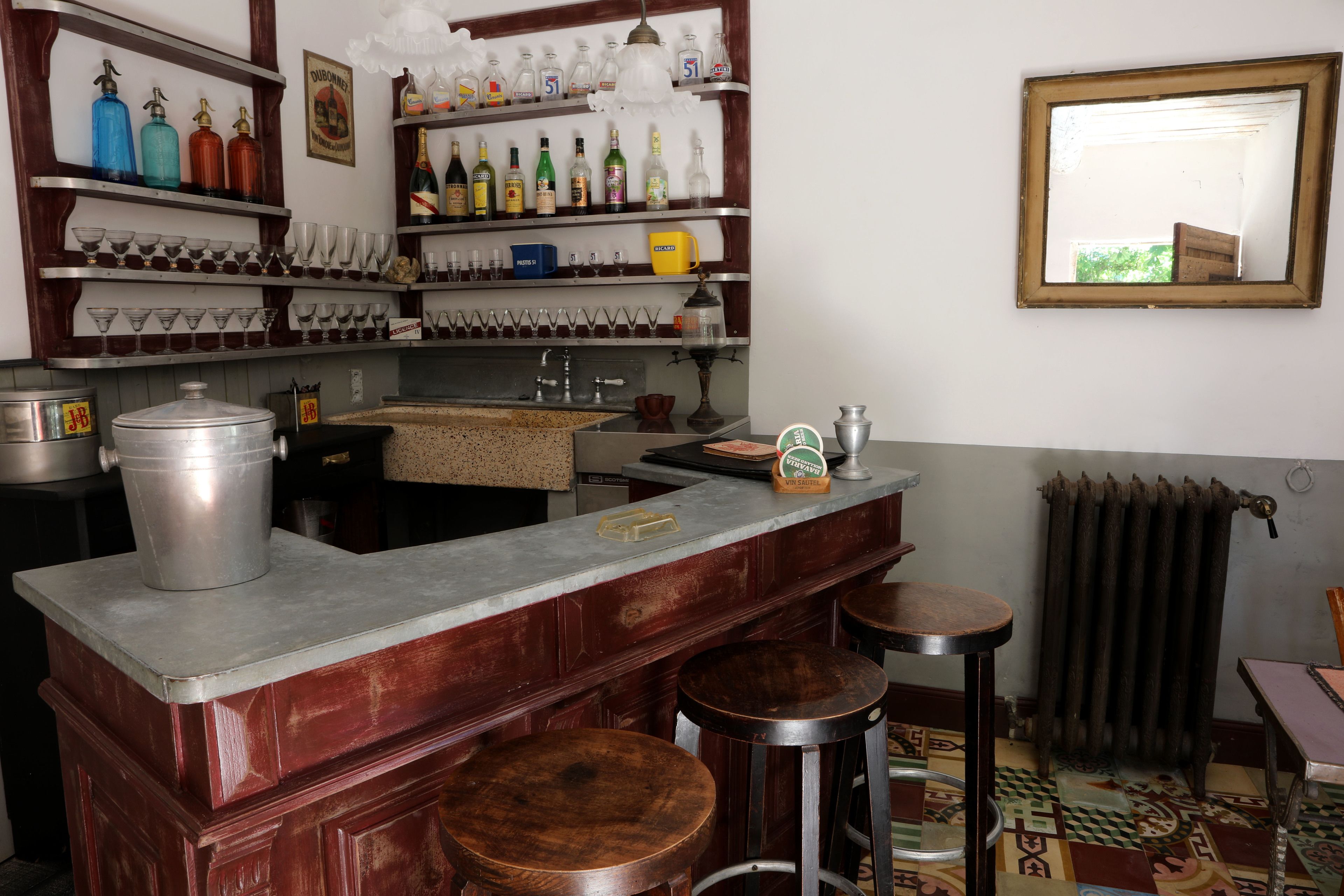 Un espace bar avec des tabourets, des étagères remplies de bouteilles et de verres, et un radiateur.