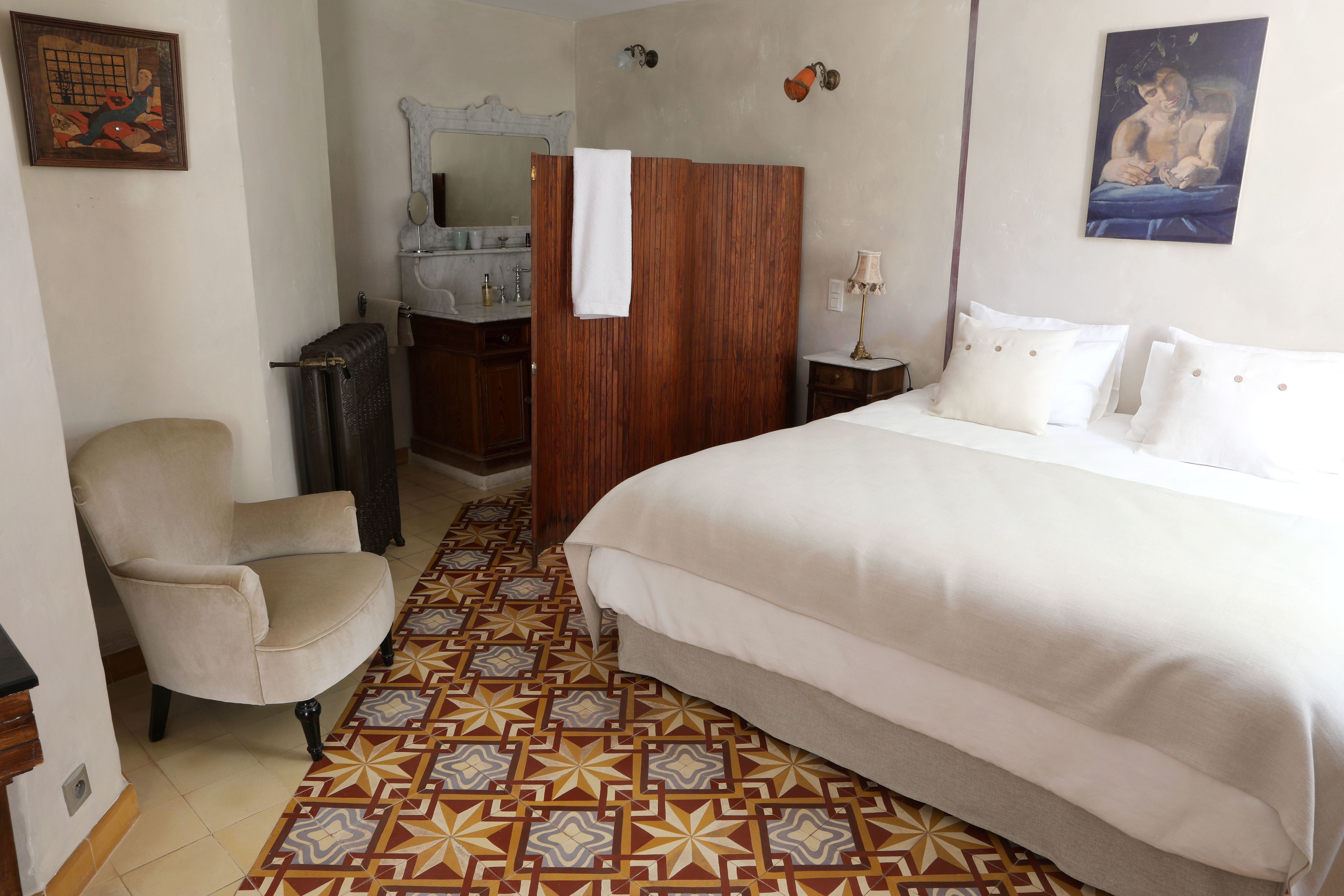 Una habitación de hotel con cama, una silla, tocador con espejo y suelo estampado.