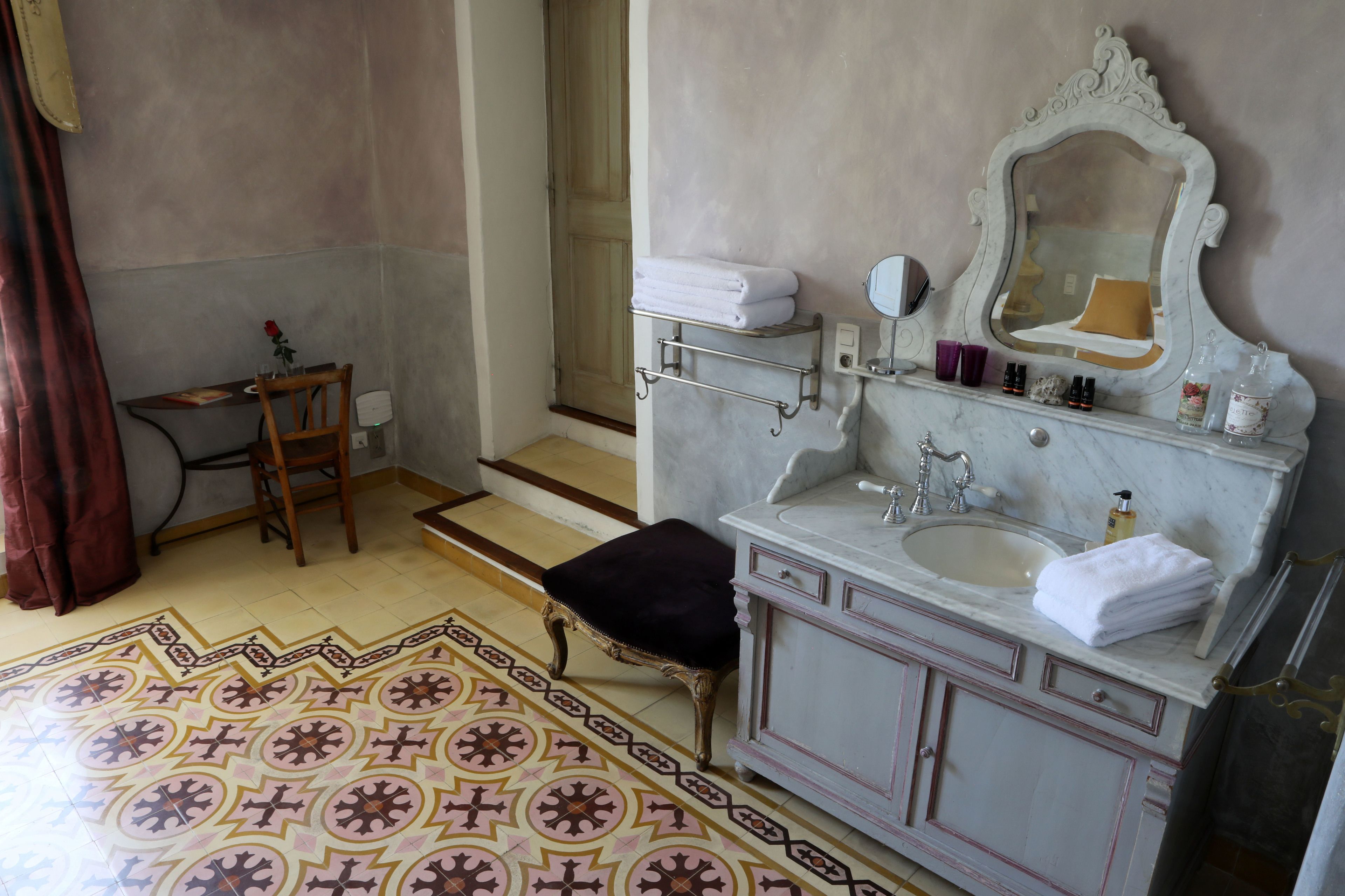 A bathroom with a marble sink, a vanity with a mirror, and a patterned floor.