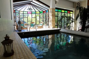 An indoor swimming pool with tiled flooring, a glass enclosure with chairs, and a lantern.