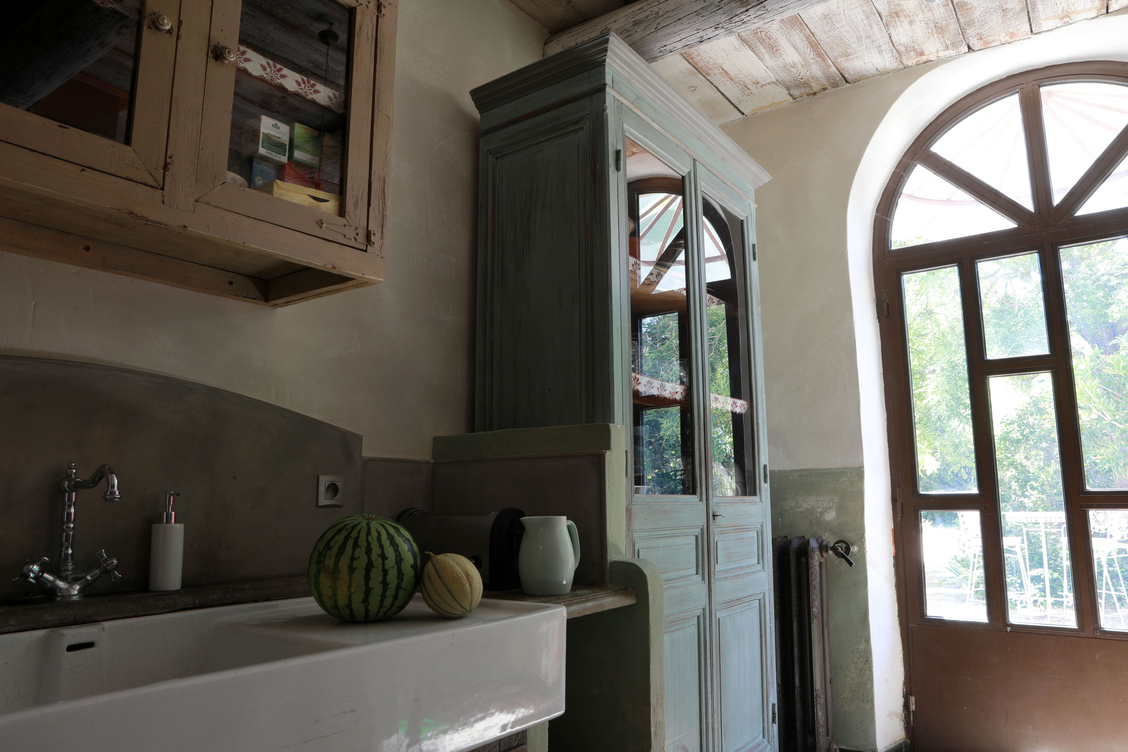 A kitchen with a wooden cabinet, a sink, and a window with a view of greenery.