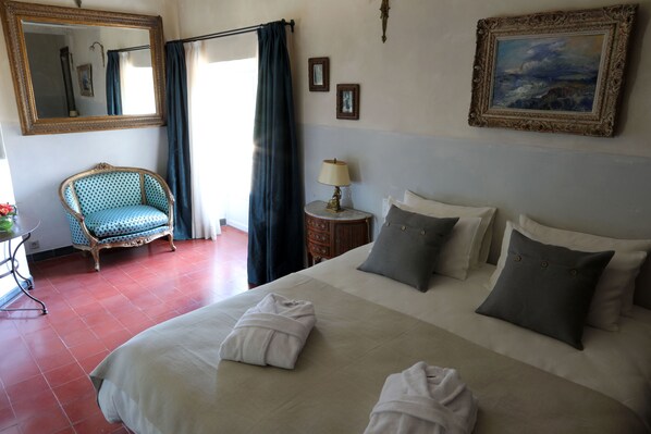 A hotel room with a large bed, a chair, a nightstand, and a painting on the wall.