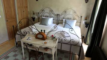 Une chambre à coucher avec un lit en métal, une porte en bois, une petite table avec une horloge et une chaise.