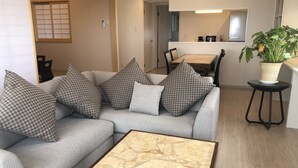 Un salón con un sofá gris, cojines estampados, una mesa de centro de madera y una planta en maceta.