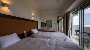 Habitación de hotel con dos camas, un ventanal grande, un balcón y vistas al mar.