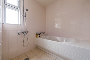 A bathroom with a bathtub, a shower, and a window. - MINATO Chatan Seaside Condominium (Chatan)