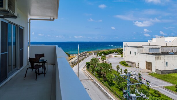 Un balcón con vista al océano, una silla y un edificio al fondo.