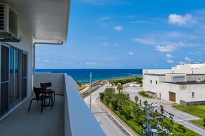 A balcony with a view of the ocean, a chair, and a building in the background. - MINATO Chatan Seaside Condominium (Chatan)