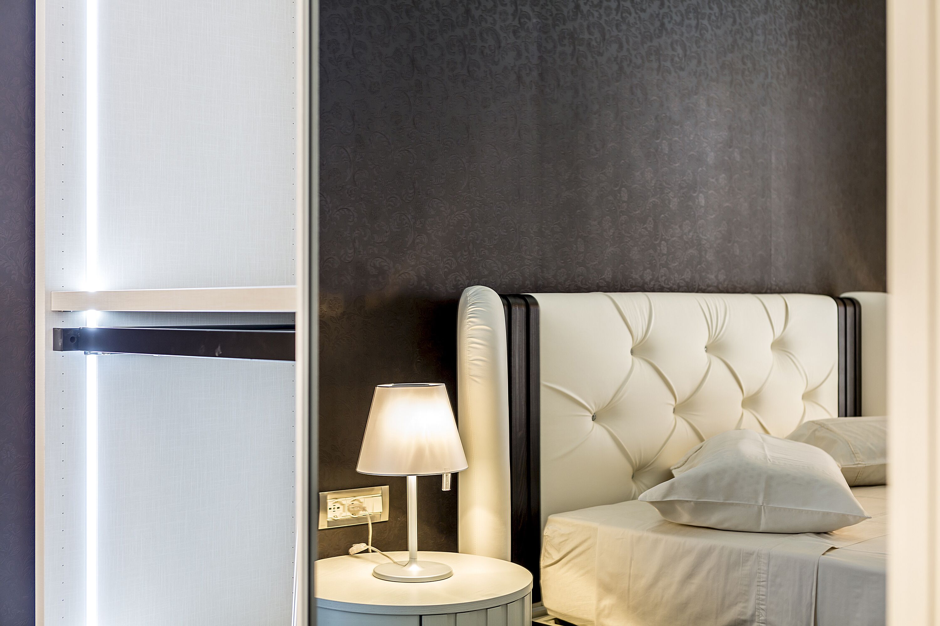 Une chambre à coucher bien rangée, avec un lit, une lampe de chevet et un luminaire fixé au mur.