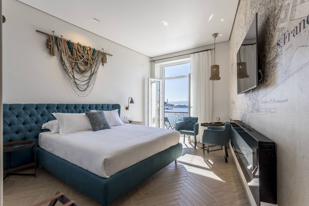 A modern hotel room with a large bed, a balcony with a view, and a wall-mounted TV.