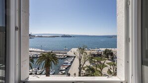 A view from a window overlooking a marina with boats docked, a large ship in the distance, and a clear blue sky. - Seaview Luxury Retreat (Split)