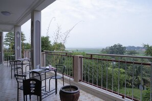 Una terraza al aire libre con mesas y sillas, una planta en maceta y vistas a un paisaje exuberante.