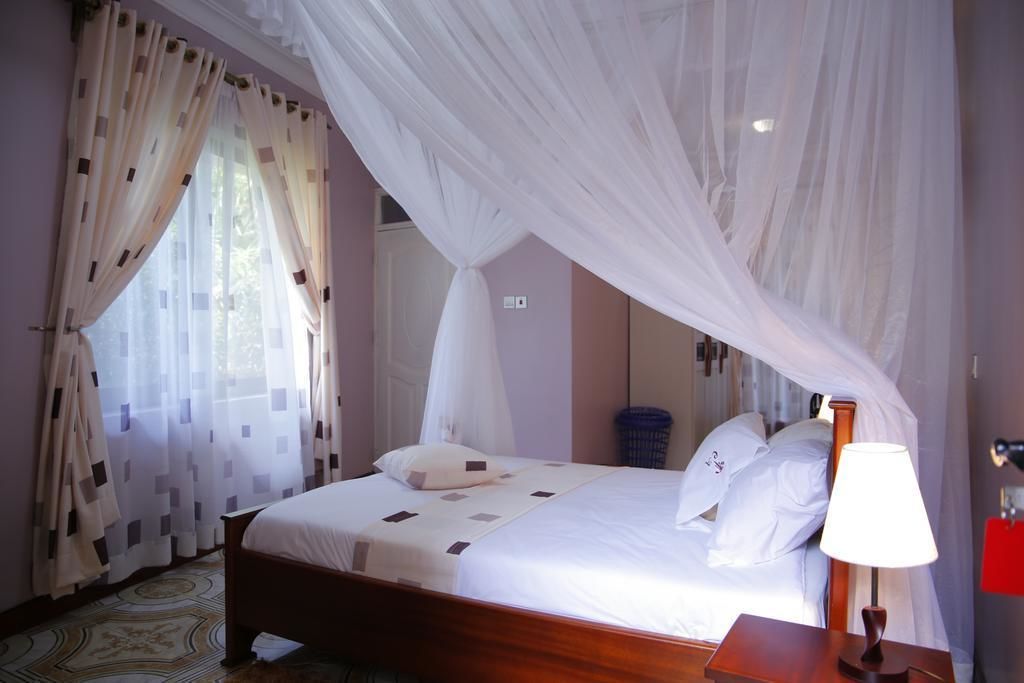 Une chambre à coucher avec un lit, des rideaux, une lampe de chevet et une fenêtre.