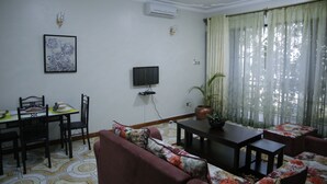 A living room with a sofa, dining table, chairs, a TV, and a potted plant. - Crystal Hotel Apartments Entebbe (Entebbe)