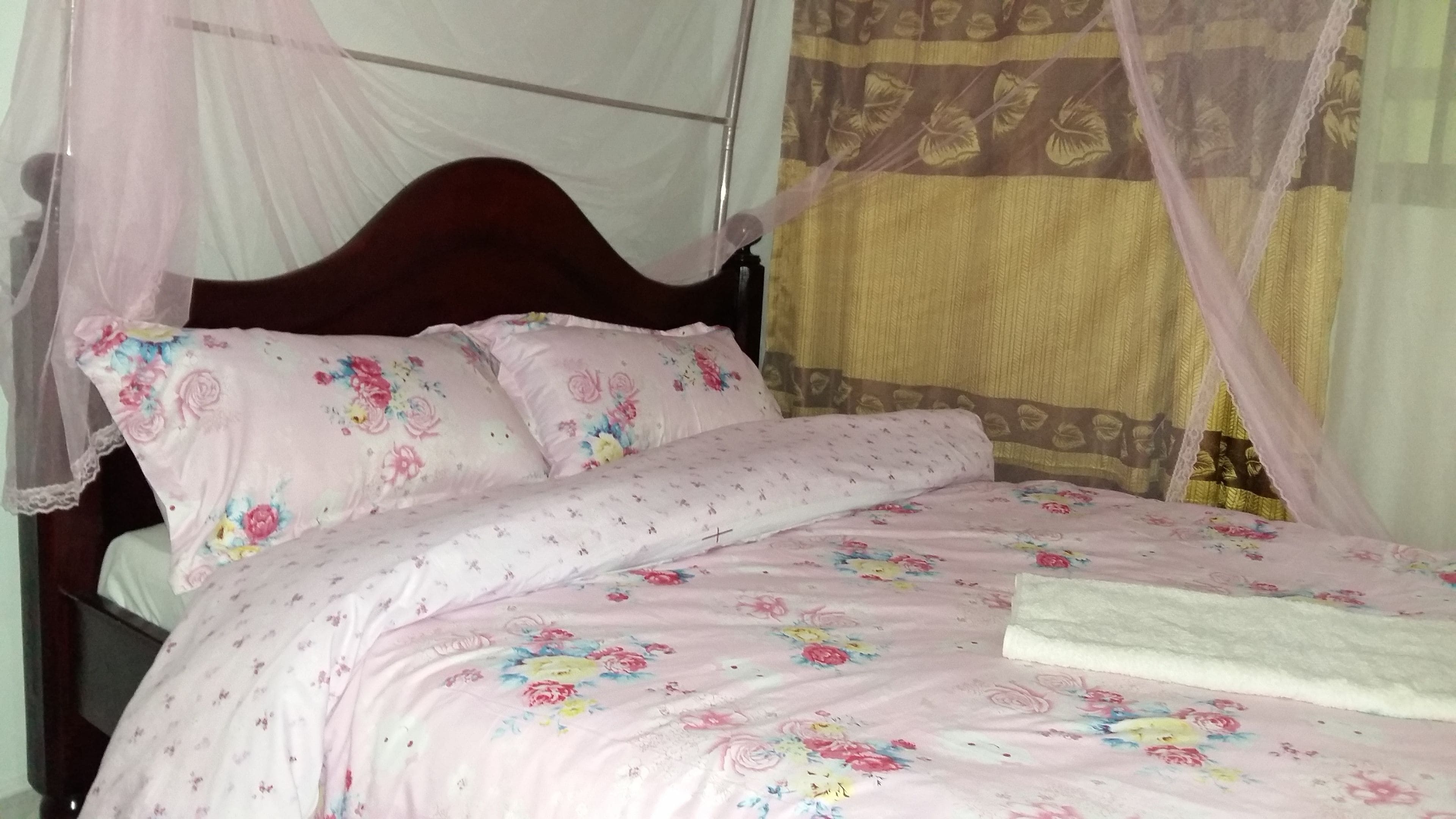 Una cama con ropa de cama estampada con flores, cabecera de madera y mosquitera.