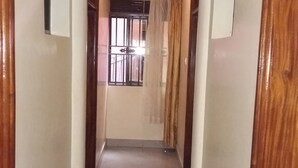 A hallway with wooden doors on either side, a tiled floor, and a window with bars at the end.