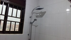 A bathroom with white tiled walls, a shower with a handheld showerhead, and a window with metal bars.