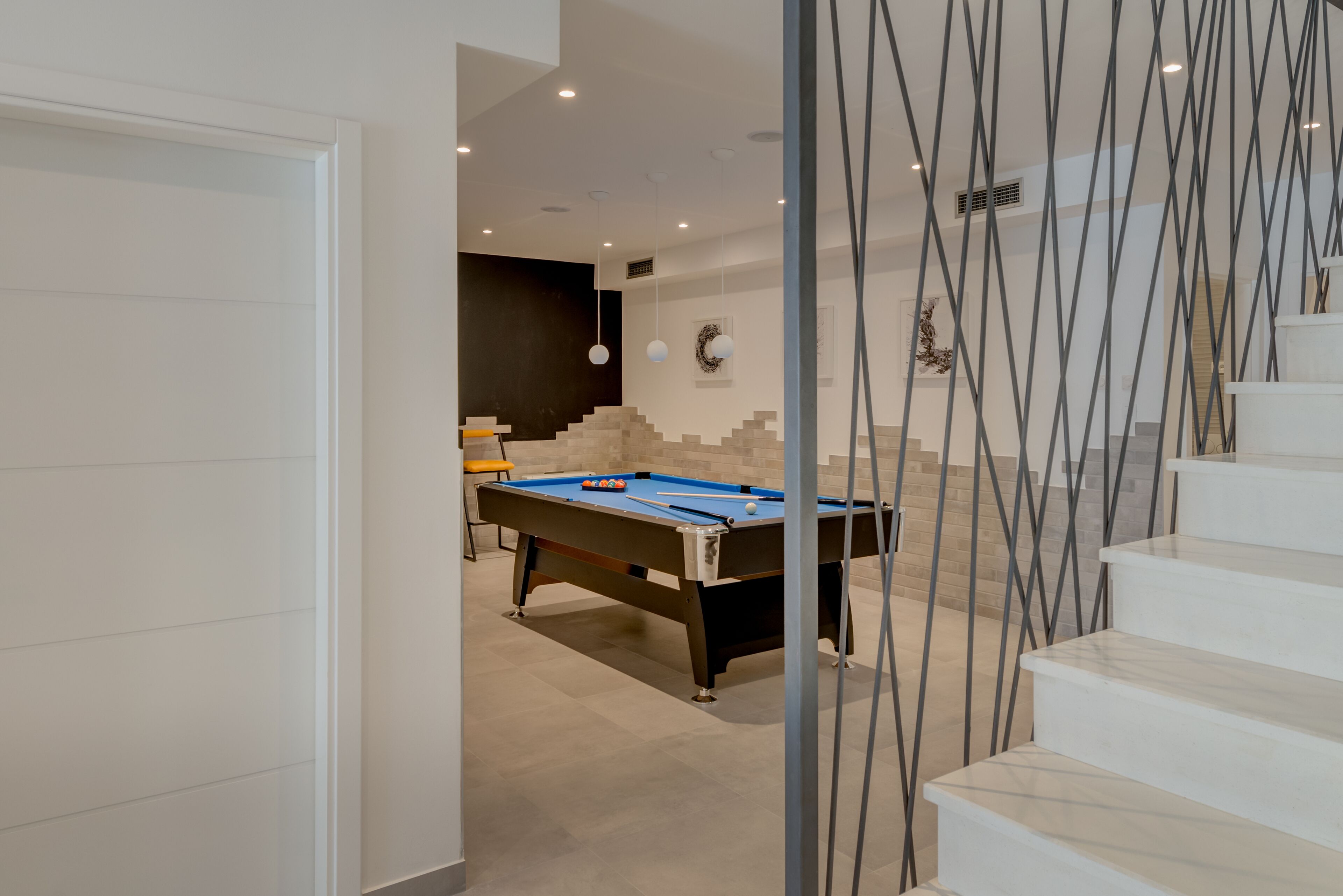 A modern indoor space with a pool table, a staircase with a unique railing design, and a wall with a decorative tile pattern.
