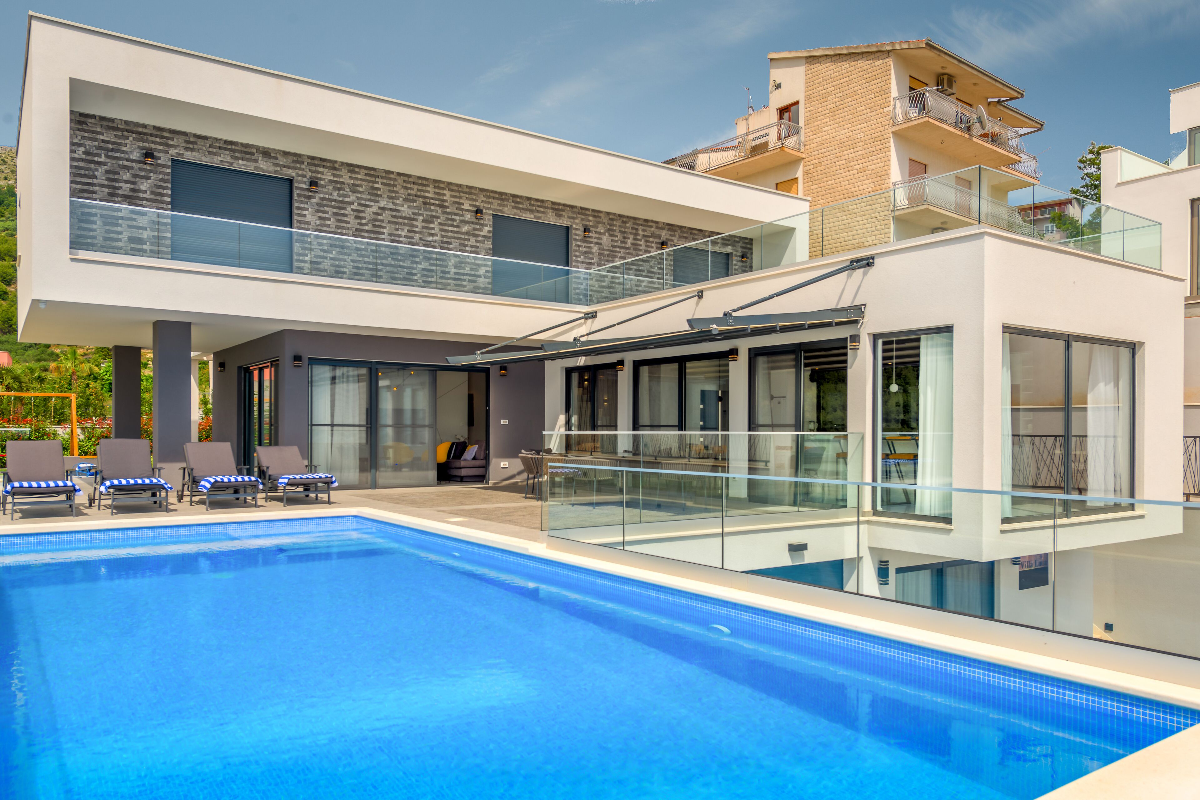 A modern two-story building with a swimming pool, glass railings, and outdoor seating.