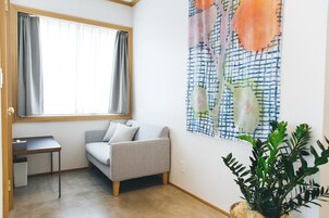 Una habitación con un sofá gris, una mesita pequeña, una planta en maceta y un cuadro abstracto grande en la pared.